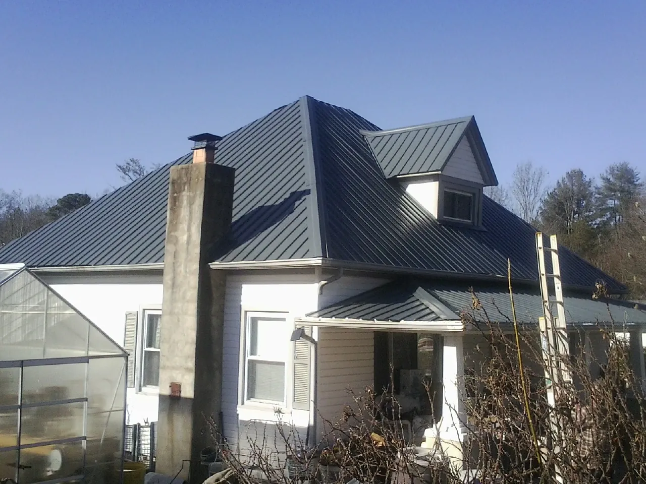 Dark blue standing seam metal roof on a white farmhouse with dormer — Slate & Tile Roof Repair by Roofing Brothers in Turtle Lake