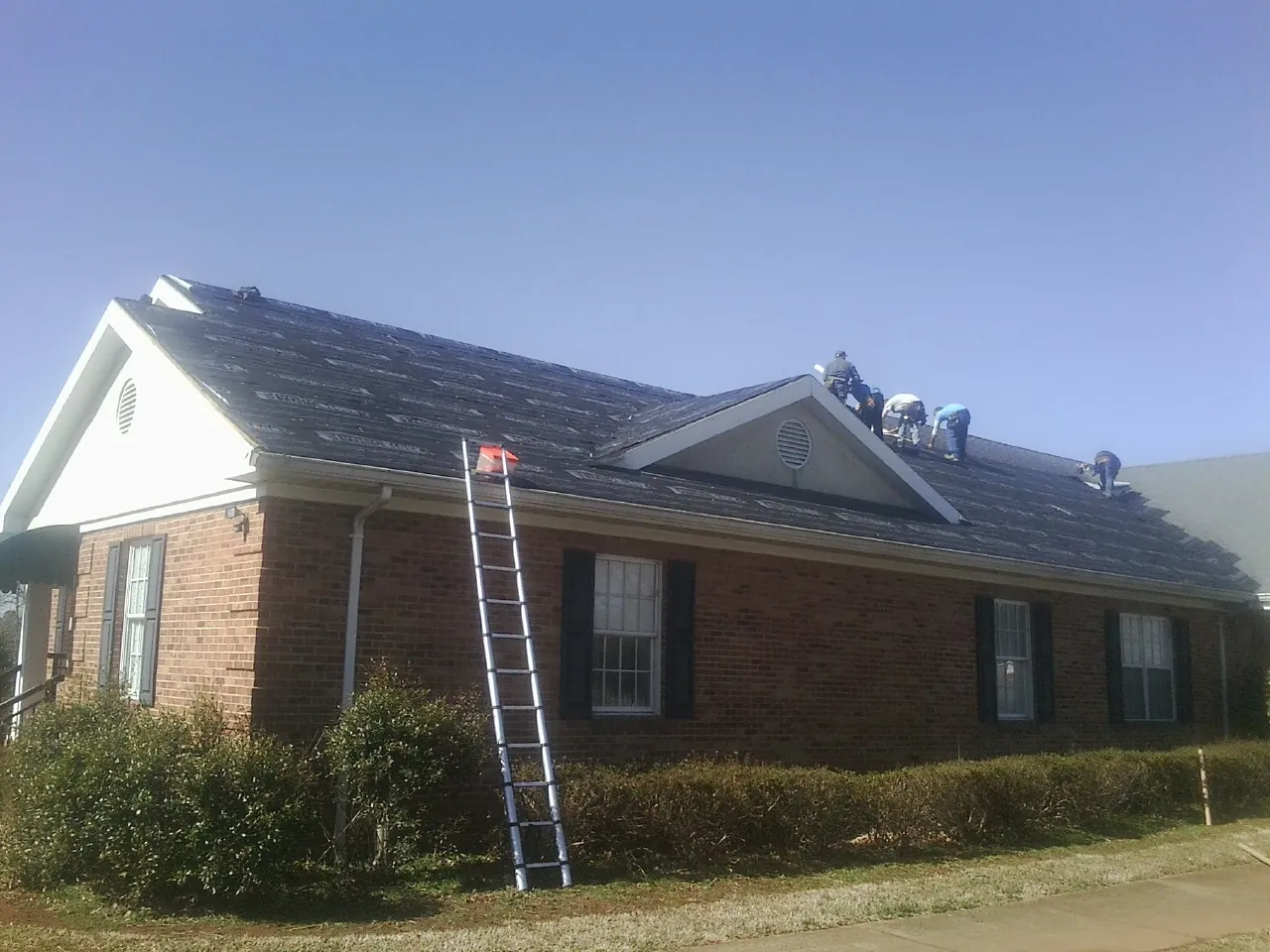 Crew tearing shingles off a brick ranch roof with a ladder set — Emergency Roof Repair work by our crew in Turtle Lake