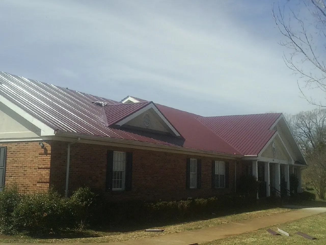 Red metal roof with gabled entries on a long brick building, from a Hail Damage Roof Repair job in Turtle Lake