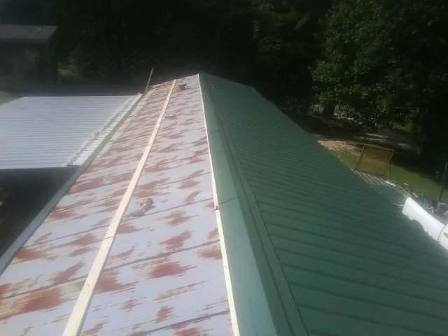 Old rusted panels beside newly installed green metal roofing — Wind Damage Roof Repair by Roofing Brothers in Turtle Lake